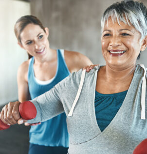Personal trainer coaching an older woman using dumbells.